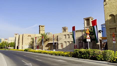 Traditional-Arab-Buildings-With-Wind-Towers-And-UAE-Flags-Along-Al-Seef-Street-In-Al-Fahidi-Historical-Neighborhood-In-Dubai