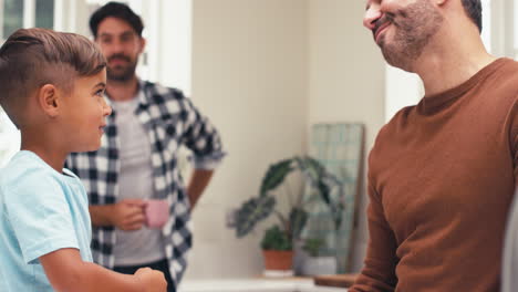 same sex family with two dads in kitchen with son sitting on counter playing rock paper scissors