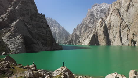 Revealing-aerial-shot-going-through-a-large-ravine-over-the-Kel-Suu-lake-in-Kyrgyzstan,-passing-over-a-man-overlooking-the-lake