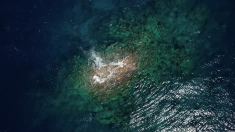 drone con una vista de arriba hacia abajo de un pináculo de roca acaba de romper el servicio rodeado por un arrecife de coral