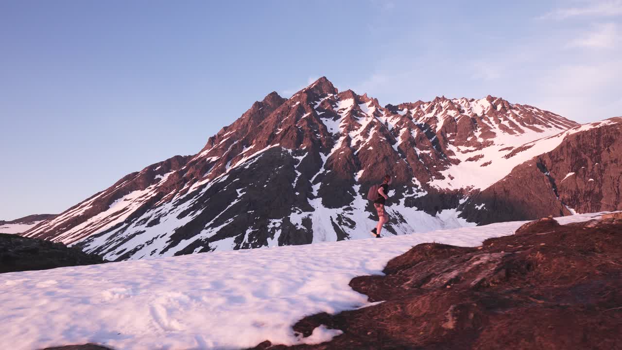 Man walking up hill through snow in a beautiful mountain scenery, climbing towards the top. Shot taken from profile of man. Norway.