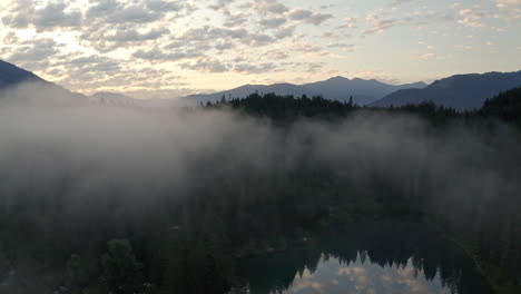 thick fog above lush pine forest and lake of caumasee switazerland - aerial shot