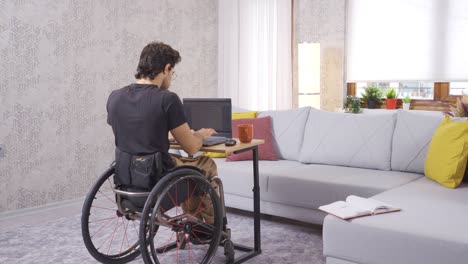 un joven discapacitado se sienta en silla de ruedas y trabaja con una computadora portátil.