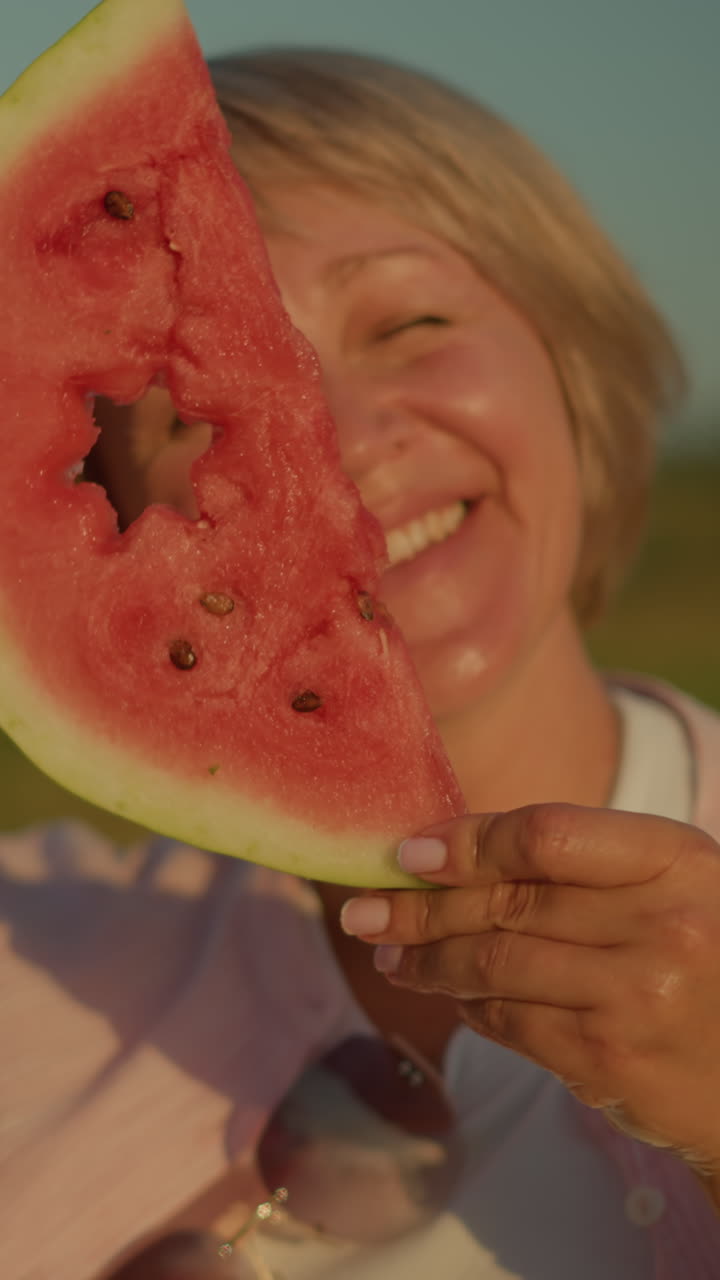mujer sosteniendo una rodaja de sandía con un recorte en forma de estrella, sonriendo e inclinando su cabeza de un lado a otro lúdicamente, el fondo borroso verde mejora el verano