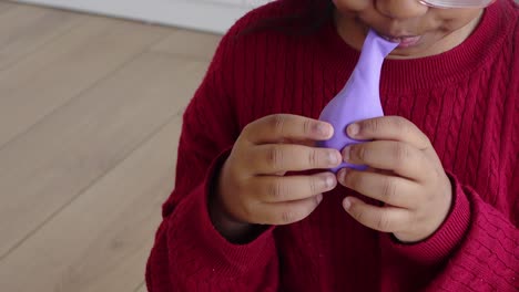 child blowing a purple balloon