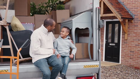 father and son sitting on tailgate of removal truck on moving day