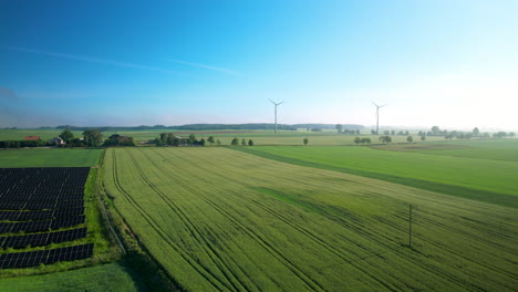 aerial panoramic shot showing agricultural fields with installed solar panel farm and windmills for clean green energy