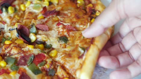 hand holding a slice of pizza with various toppings
