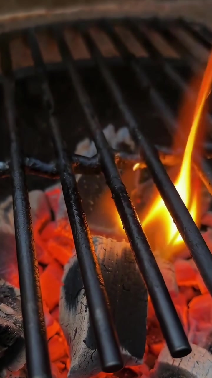 Fiamme che si alzano da braci ardenti su una griglia da barbecue vuota.