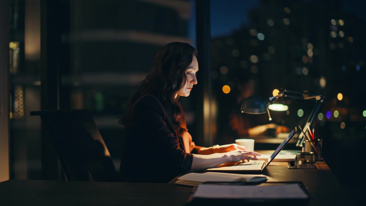 Overworked woman typing laptop staying late at evening office workspace closeup