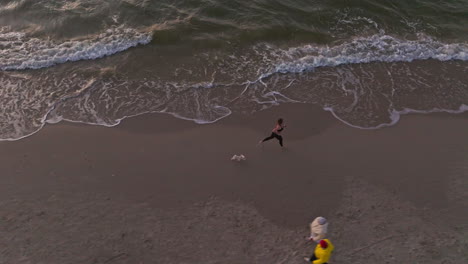 tracking drone shot of woman running with a dog on sandy beach during the day, outdoor