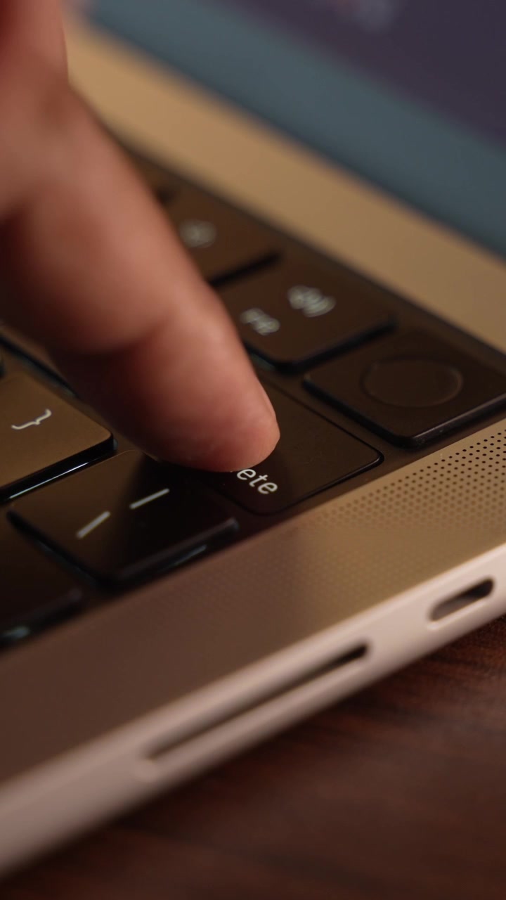 Finger trykker på sletteknappen på et bærbart tastatur i et varmt oplyst rum