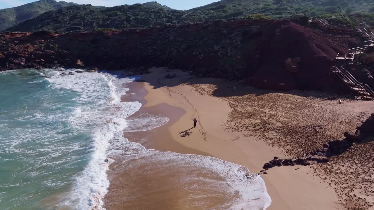вид с беспилотника на человека, выгуливающего собаку вдоль пляжа с горами в испании