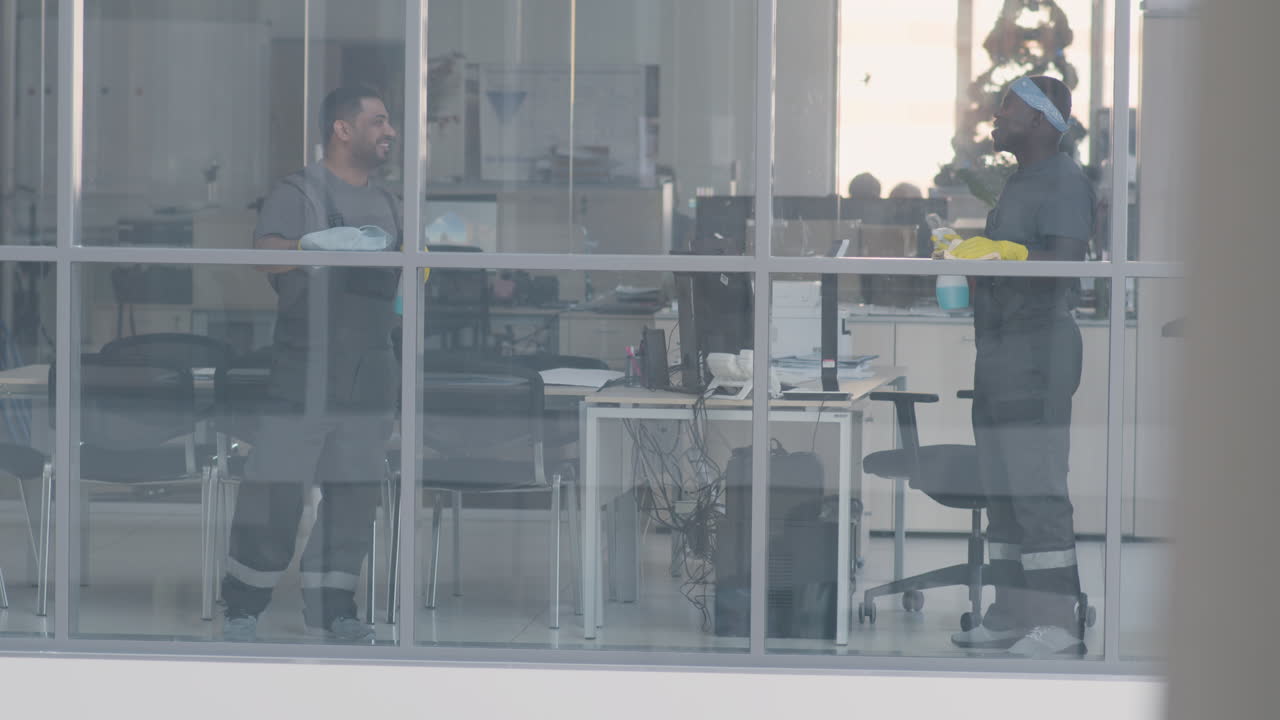vista desde el exterior y un hombre de limpieza árabe hablando y limpiando los cristales de las ventanas dentro de una oficina