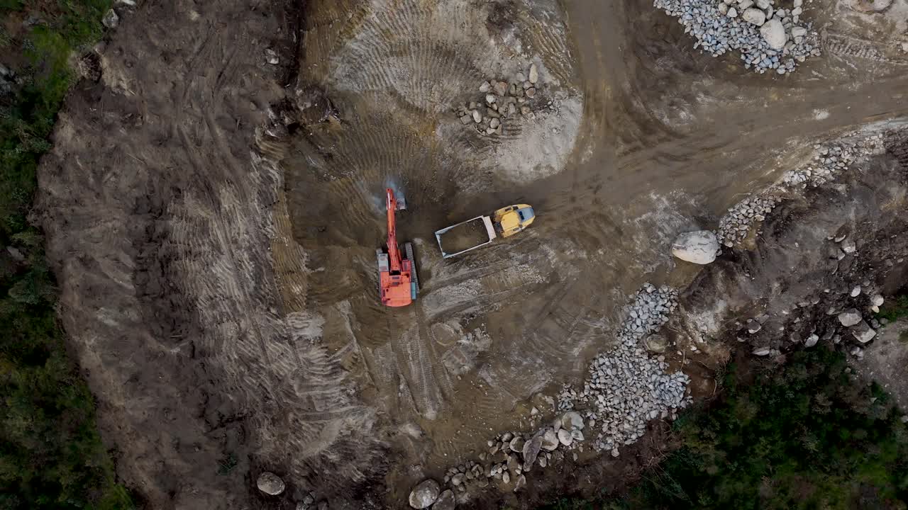 Aerial excavator fills truck with sand on rocky construction site in Portugal