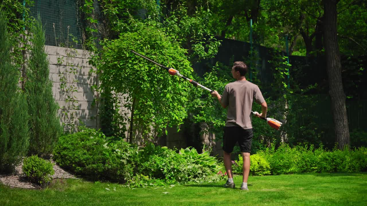 Man Trimming Tall Bush with Hedge Trimmer in Green Garden