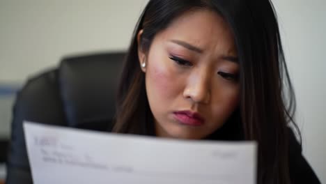 a woman sits at her desk, reviewing important documents with a concerned expression. the atmosphere conveys tension and focus as she processes the information in front of her.