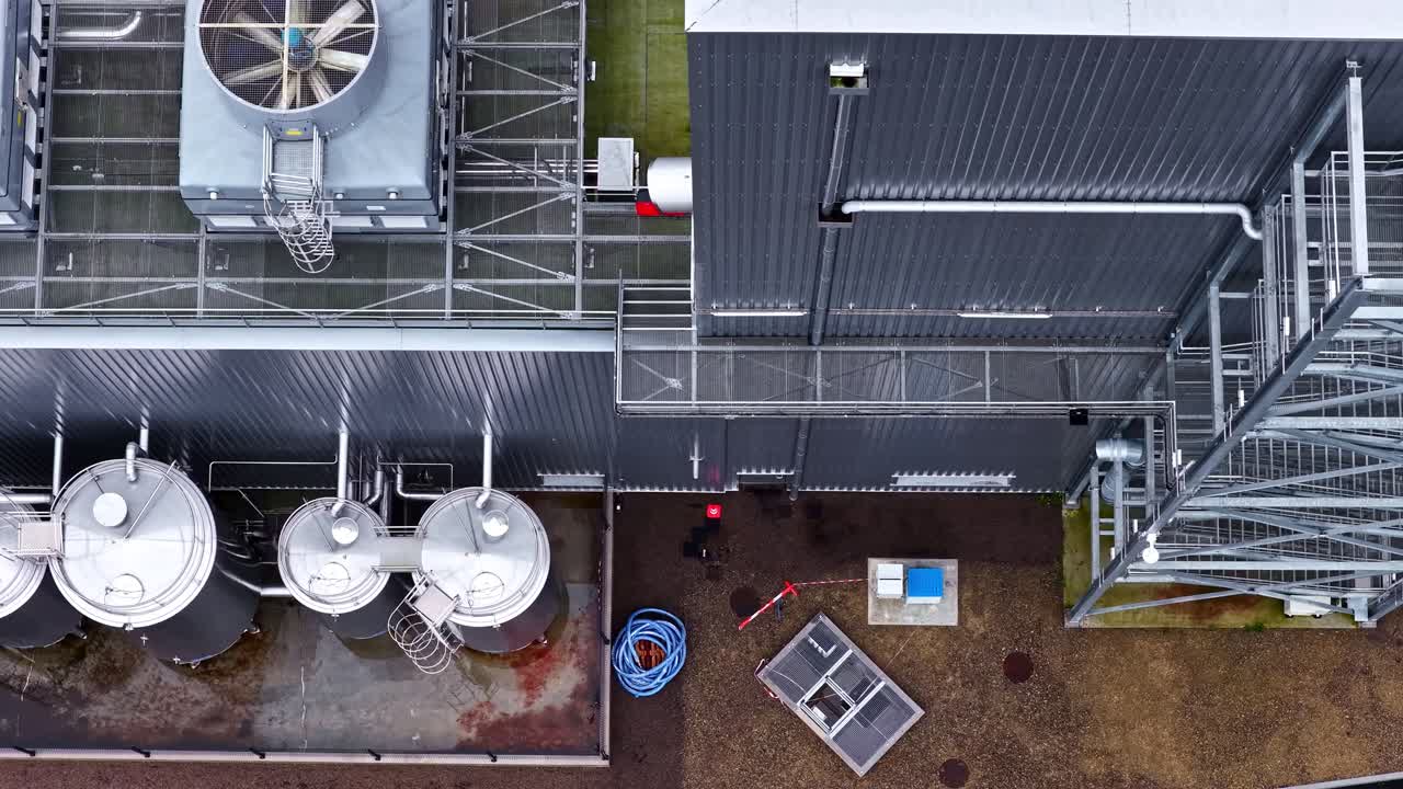 Luftfoto fra drone, der flyver over taget på en fødevareforarbejdningsvirksomhed i Letland, viser store køleventilatorer, tårne, rustfri tanke, rørsystemer, platforme og industrielt anlæg