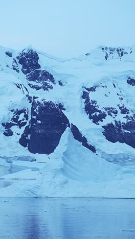 antarctica blue icebergs and mountains, iceberg floating on ocean sea water in vertical video for social media, instagram reels and tiktok, antarctic peninsula winter ice seascape landscape scenery