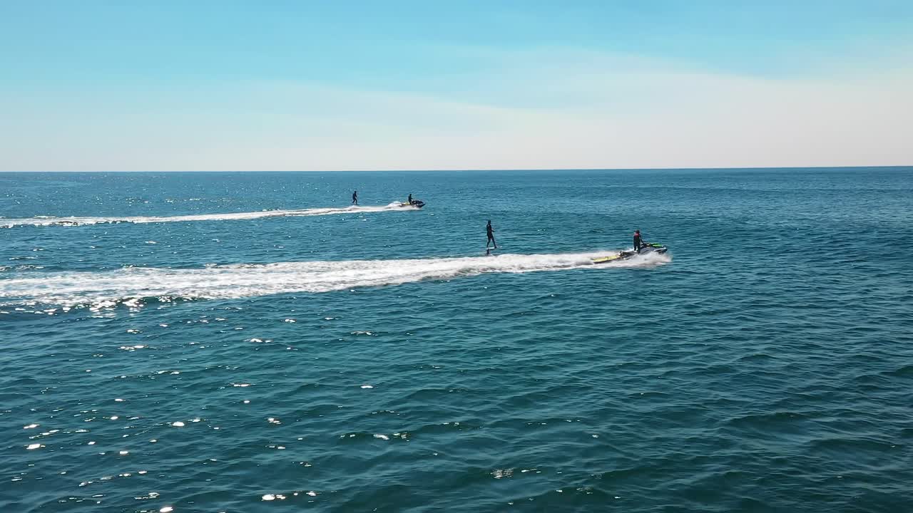 Jet ski towing athletes hydro foiling on the ocean on blue summer's day in Sydney, NSW, Australia. Water sports aerial.