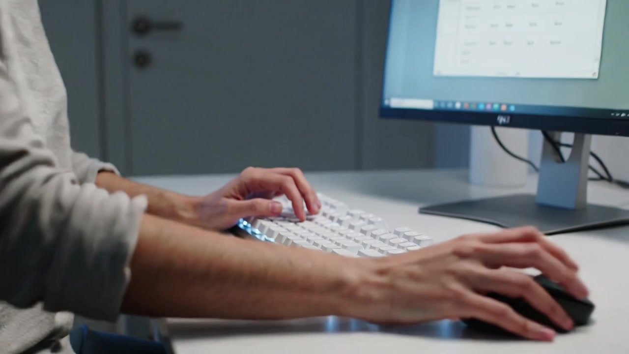 Typing user in long-sleeve top switching from keyboard red keycap to mouse at desk editing grid