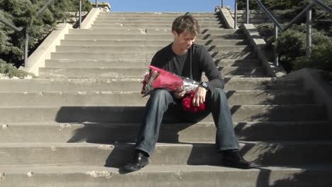 Ein-Mann-Wartet-Auf-Der-Treppe-Mit-Blumen-Und-Einem-Teddybären