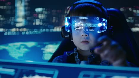 child gamer using augmented reality glasses and headphones is playing videogame using holographic interface and touching virtual screen with his finger in futuristic command center