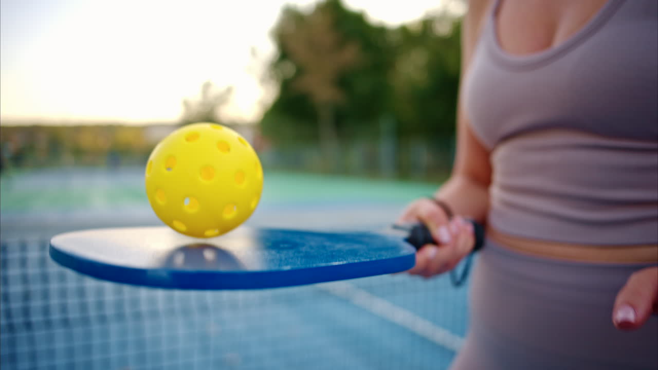 Woman playing pickleball with yellow ball and blue paddle at a court