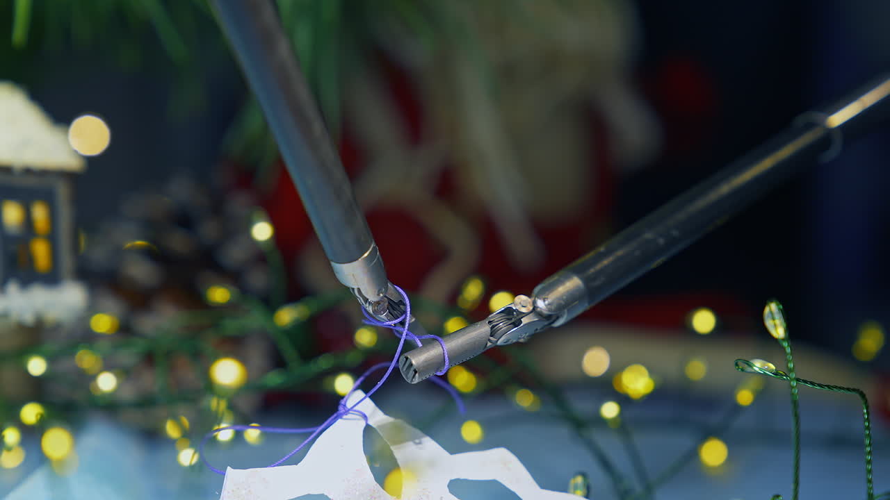 Tiny forceps of Da Vinci system tying a knot on a thread. Fastening the thread on the paper snowflake by robotic arms of Da Vinci surgical system. Close up.
