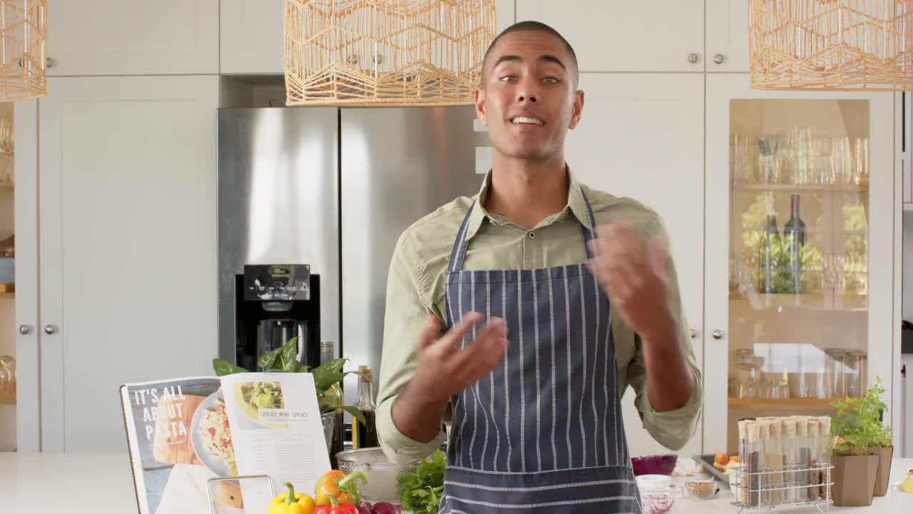vlogger de cocina masculino biracial en delantal hablando y filmando en la cocina