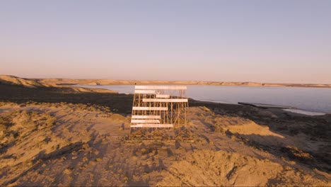 Old-Beacon-Signal-Against-Warm-Sunlight-At-The-Coast-Of-Golfo-Nuevo-In-Peninsula-Valdes,-Patagonia,-Argentina---pullback-drone-shot