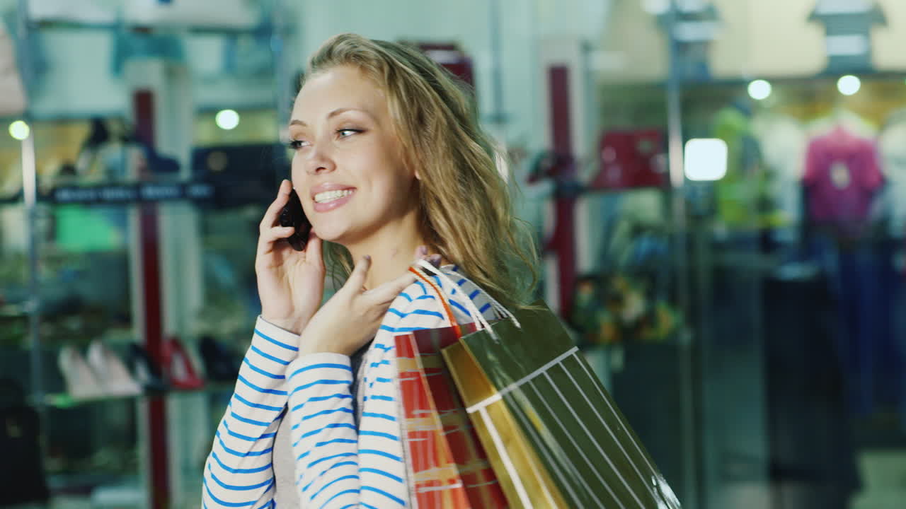 그것은 유리 sh의 배경에 대해 전화 통화하는 쇼핑백과 매력적인 여자