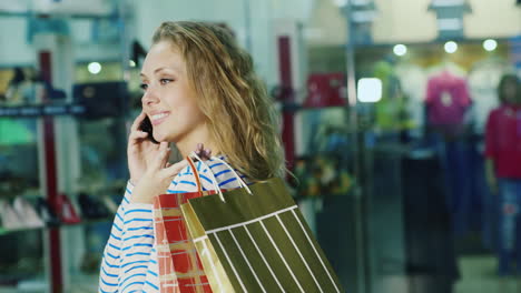 una mujer atractiva con bolsas de compras hablando por teléfono está contra el fondo de vidrio sh