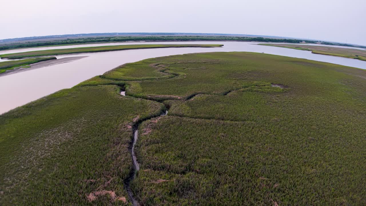 Drone footage capturing Charleston, South Carolina’s marshland peninsula with a wide river on one side and winding tidal creek on the other at dusk