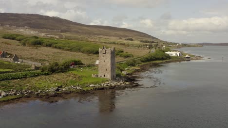 aerial orbit around stone tower house reflecting in calm water below, cloudy day
