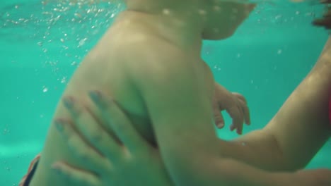 cute blonde toddler is swimming under the water in the swimming pool until his mother helps him to get out. and underwater shot