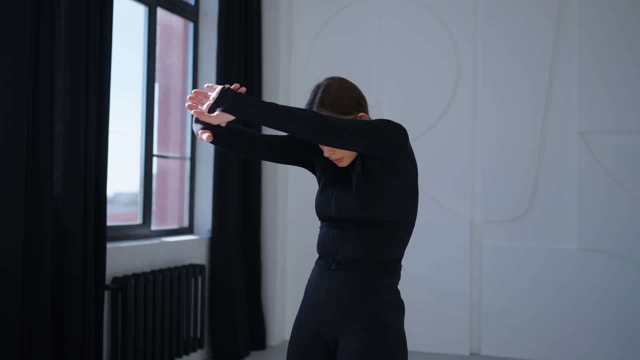 검은 옷을 입은 여자가 스튜디오에서 춤을 추면서 팔을 고 있다.