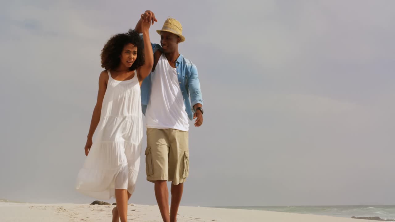 vista frontal de una pareja afroamericana caminando de la mano en la playa 4k