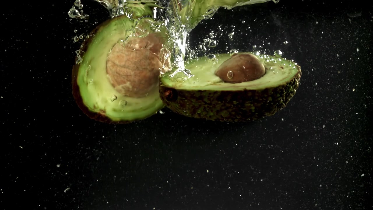Metà di avocado fresco che si tuffano nell'acqua al rallentatore