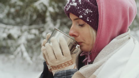 young woman drinking hot tea outdoors on winter day