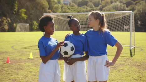holding soccer ball, three girls in school uniforms standing on field
