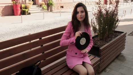 pretty brunette in pink sitting on a bench with a disk in the city