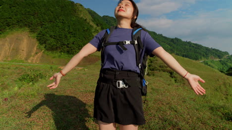 medium view pan up along woman raising arms out relaxing and feeling the breeze on long trek hiking