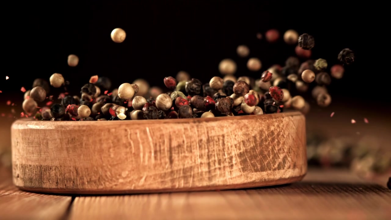 Grani di pepe assortiti che cadono in una ciotola di legno rustica