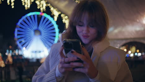 woman photographing luna park ferris wheel on cellphone closeup. happy lady