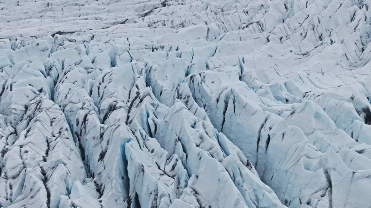 Vista rotante da drone di profonde fessure in un ghiacciaio islandese striato di cenere nera.