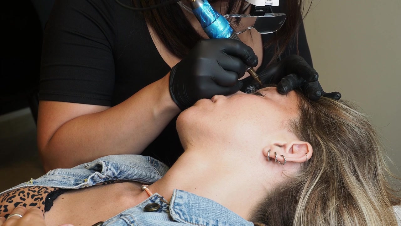 Eyebrow tattooing procedure with permanent makeup machine, pigment and gloves in beauty salon