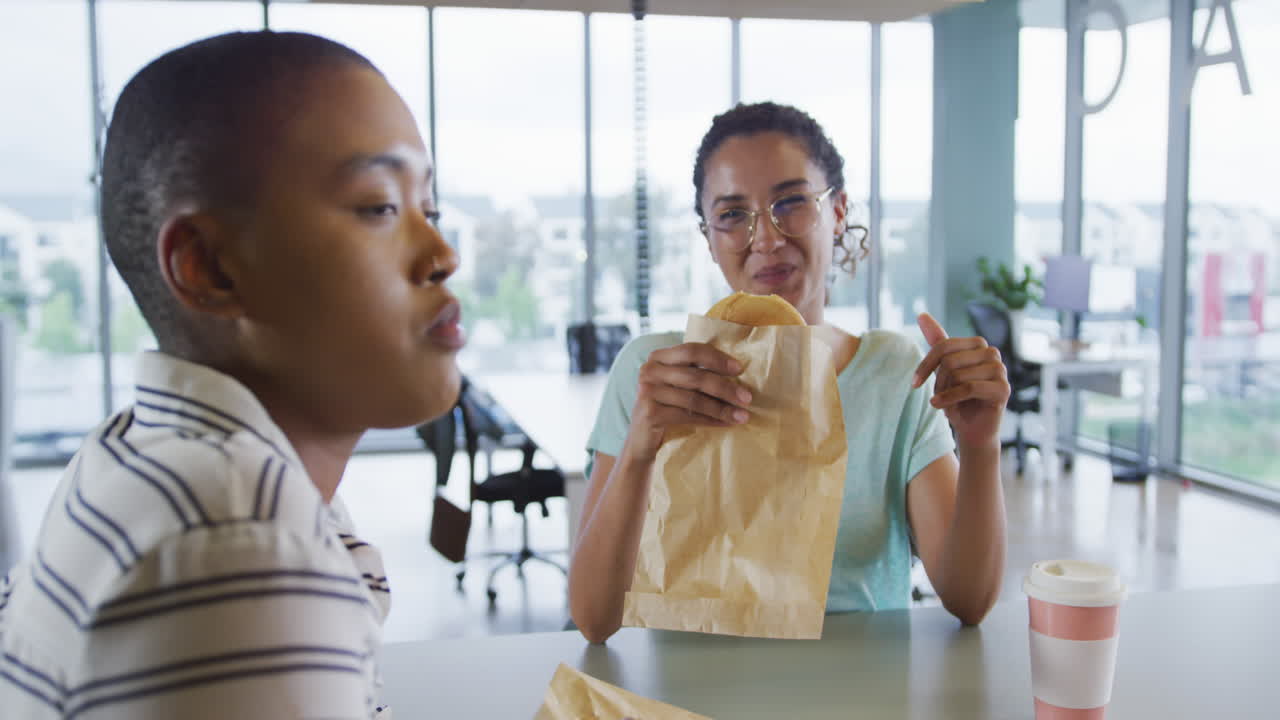 diversas compañeras creativas comiendo y hablando en la cantina del lugar de trabajo
