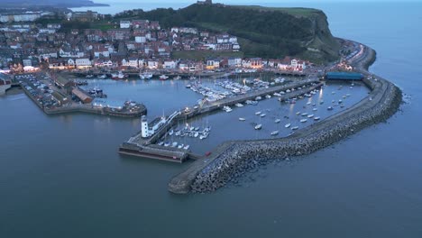 Toma-Aérea-Hacia-Atrás-Del-Puerto-De-Scarborough-Con-Barcos-En-El-Océano-Durante-La-Puesta-De-Sol-En-Diciembre-En-Scarborough,-Inglaterra