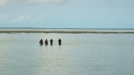 Grupo-De-Aldeanos-Africanos-Vadeando-El-Océano-En-Marea-Baja-Para-Recolectar-Comida-De-Mar,-Mujeres-Hablando
